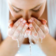 Beautiful young woman washing her face splashing water in a home bathroom.