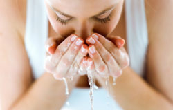 Beautiful young woman washing her face splashing water in a home bathroom.