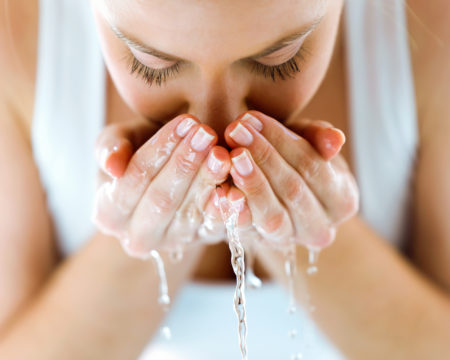 Beautiful young woman washing her face splashing water in a home bathroom.