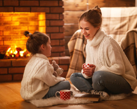 family mother and child drinking tea and laughing on winter evening by fireplace