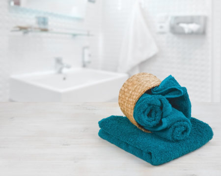 Green-blue folded towels in wicker basket over defocused bathroom