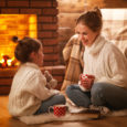family mother and child drinking tea and laughing on winter evening by fireplace