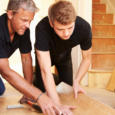 Two men laying wood panel flooring in a house