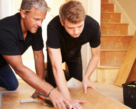 Two men laying wood panel flooring in a house