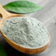 Close-up of a cosmetic dry gray clay in a wooden spoon on a black wooden table. Decorated with green leaves.