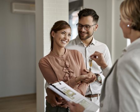 Young happy couple receiving keys of their new home from real estate agent.