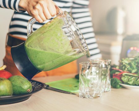 woman's hand pouring green smoothie into a glass