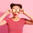 Close-up portrait of her she nice cute attractive glamorous funny cheerful cheery girl wearing striped t-shirt covering closing eyes with colorful snacks isolated over pink pastel background